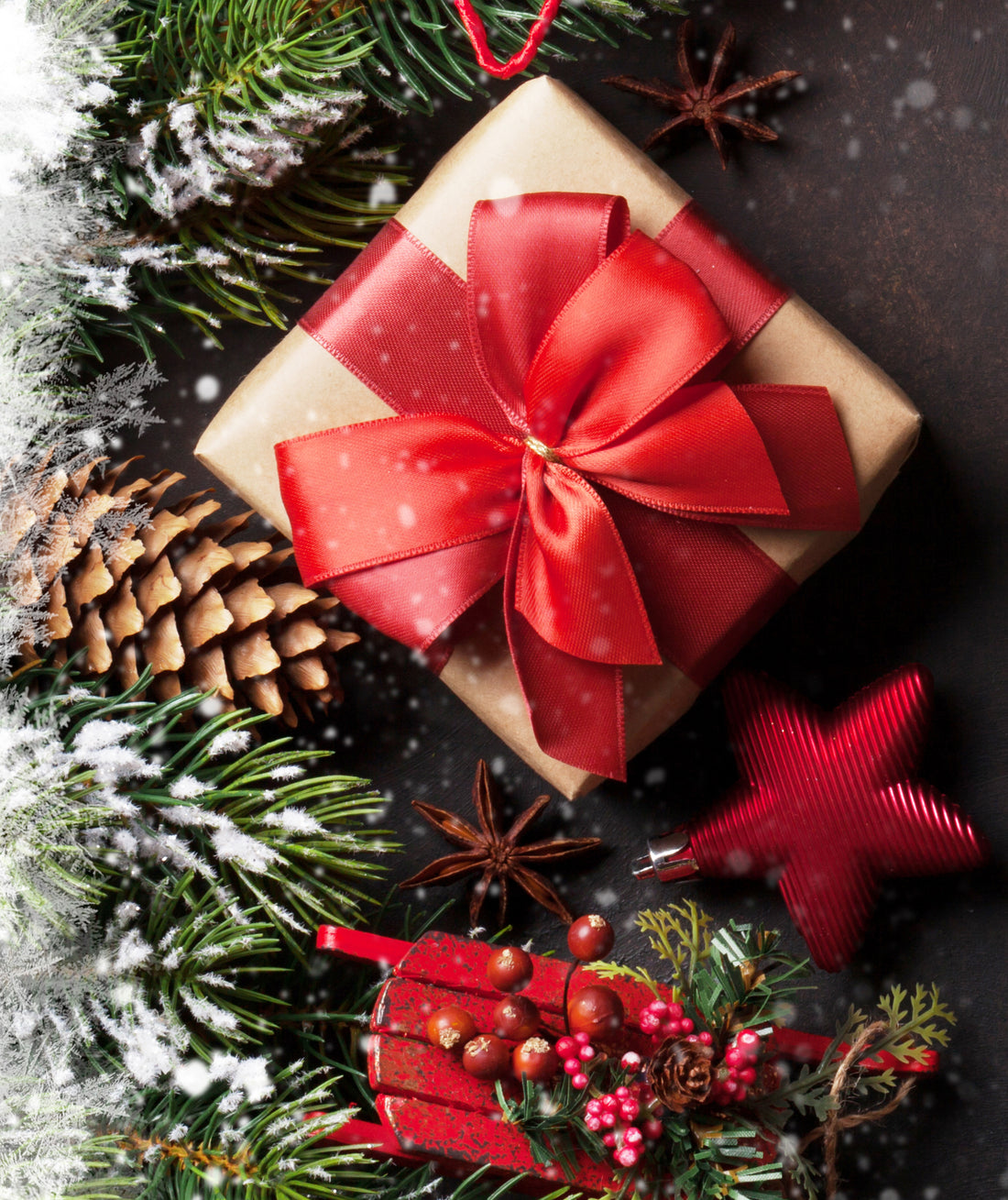Wrapped gift with a large red bow among evergreen branches and pinecones.