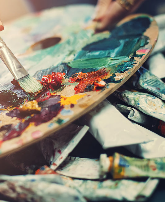Paint-covered wooden palette with brushes and vivid blobs of color.