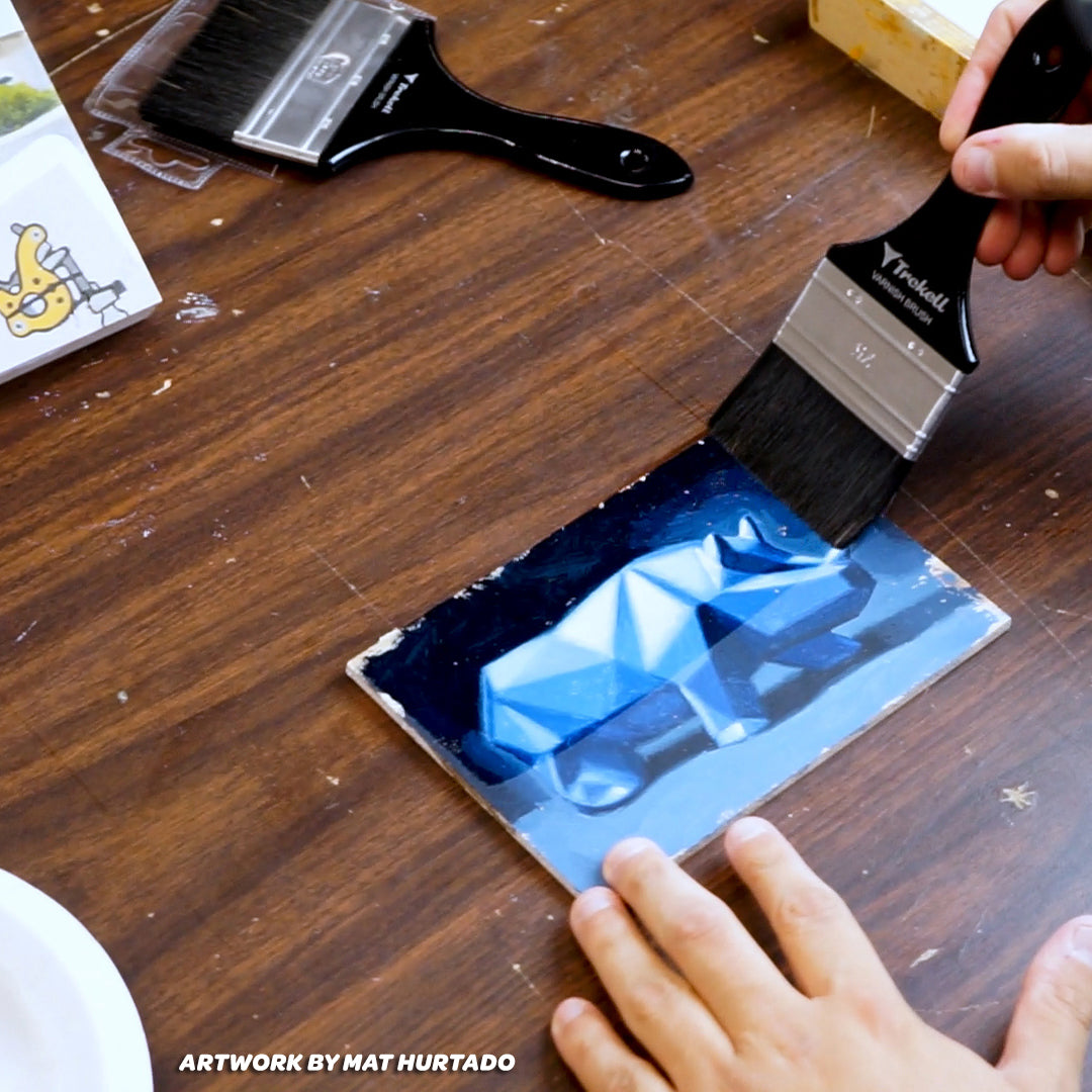 Hand applies varnish to a blue geometric painting with a wide brush.