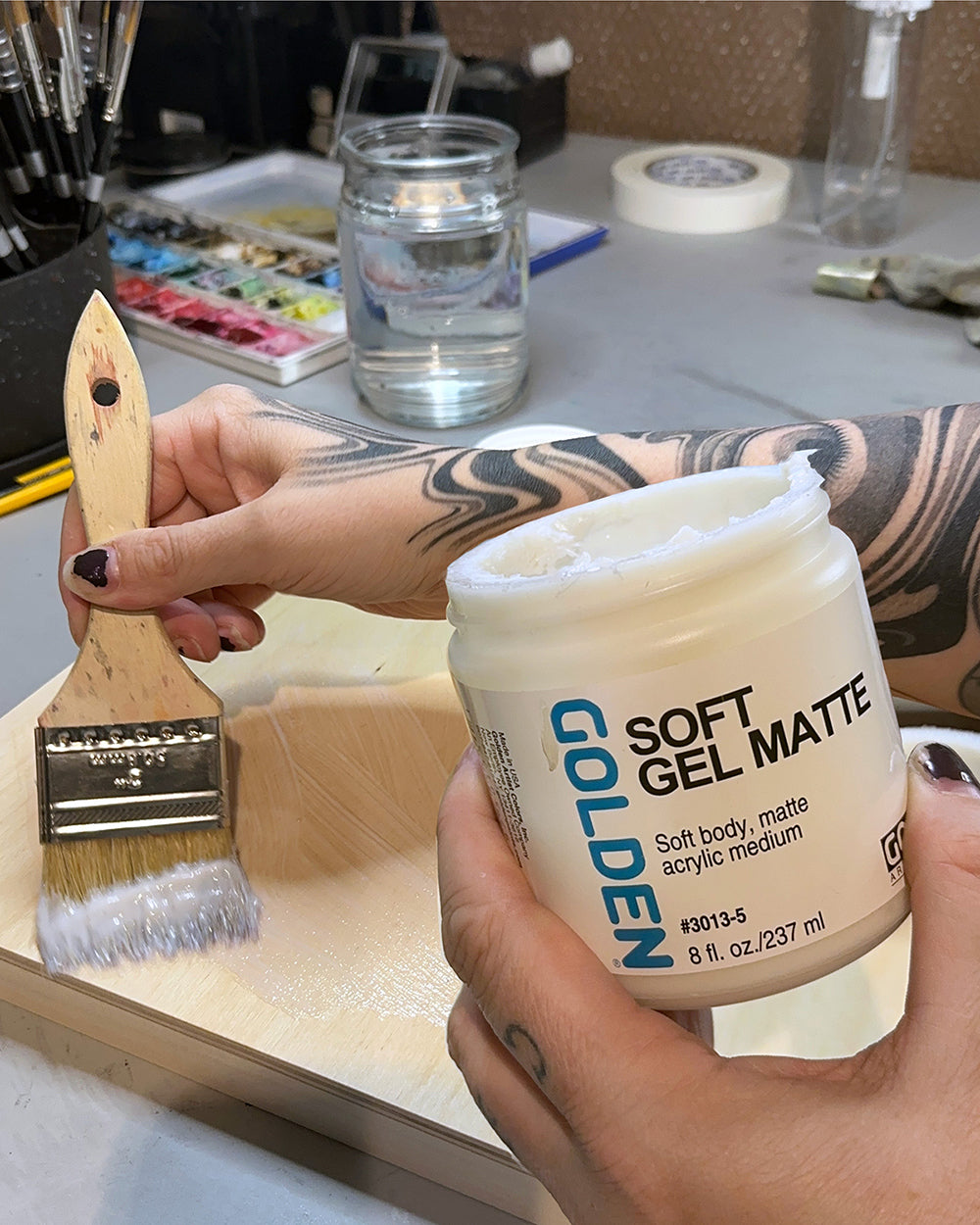 Hand holds Golden Soft Gel Matte beside a brush and white panel.