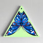 Blue butterfly painted on a lime-green triangular panel with a hanging hole.