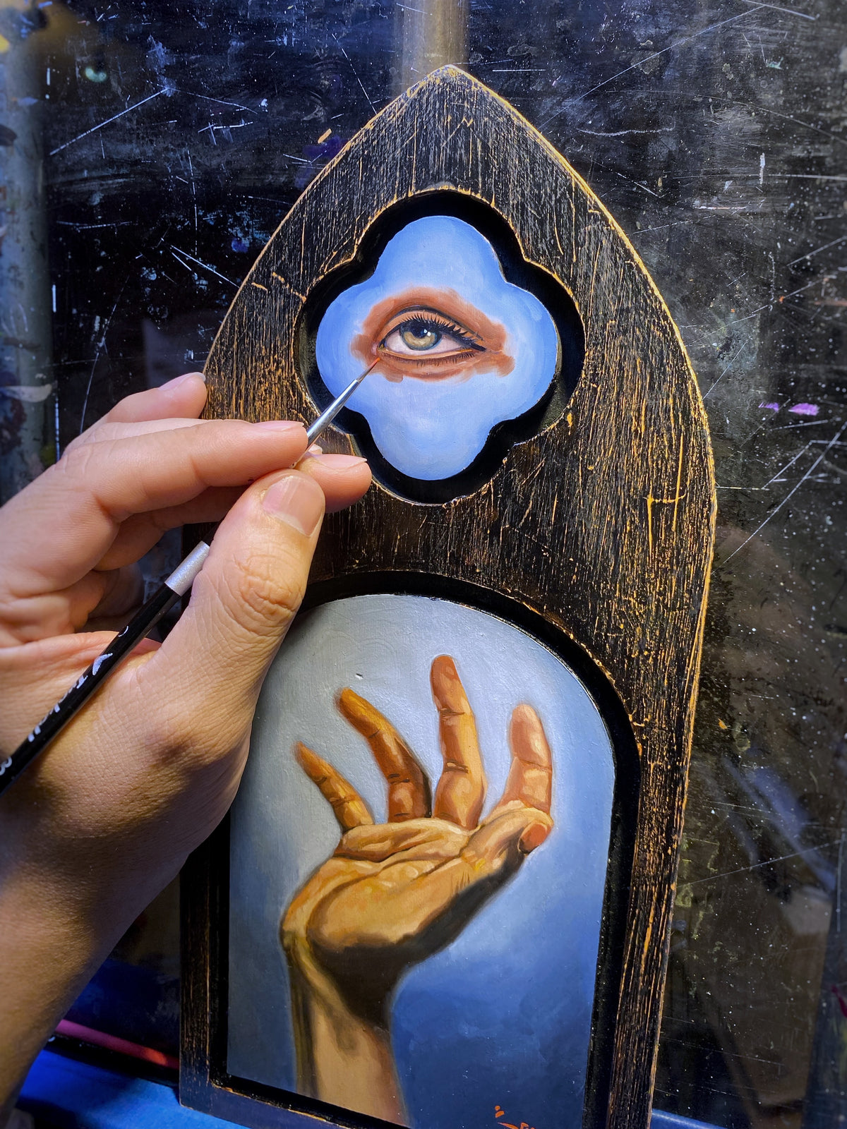 Hand paints an eye on blue above a golden hand on a black-and-gold Trekell Gothic Vienna Floater Panel.
