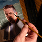 Hand holds a fine brush beside a painted portrait of a bearded man.