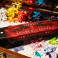 Andrew Cadima brush set box on a wooden palette covered with colorful paint.