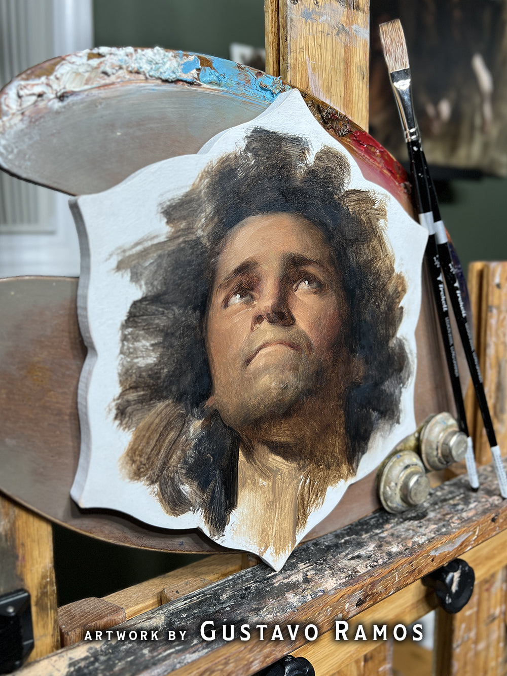 Portrait of a curly-haired man looking upward on a shaped panel, credited to Gustavo Ramos.