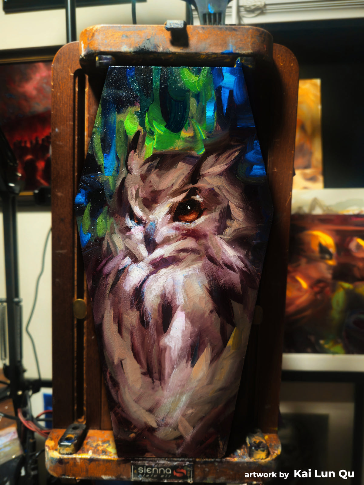 Painting of a long-haired cat on a coffin-shaped panel, with bright blue and green strokes above its head.