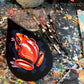 Faceted orange-and-red frog on a black raindrop panel beside brushes on a paint-covered table.