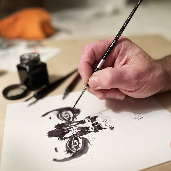 Hand paints black details in a symmetrical ink illustration using a fine brush.