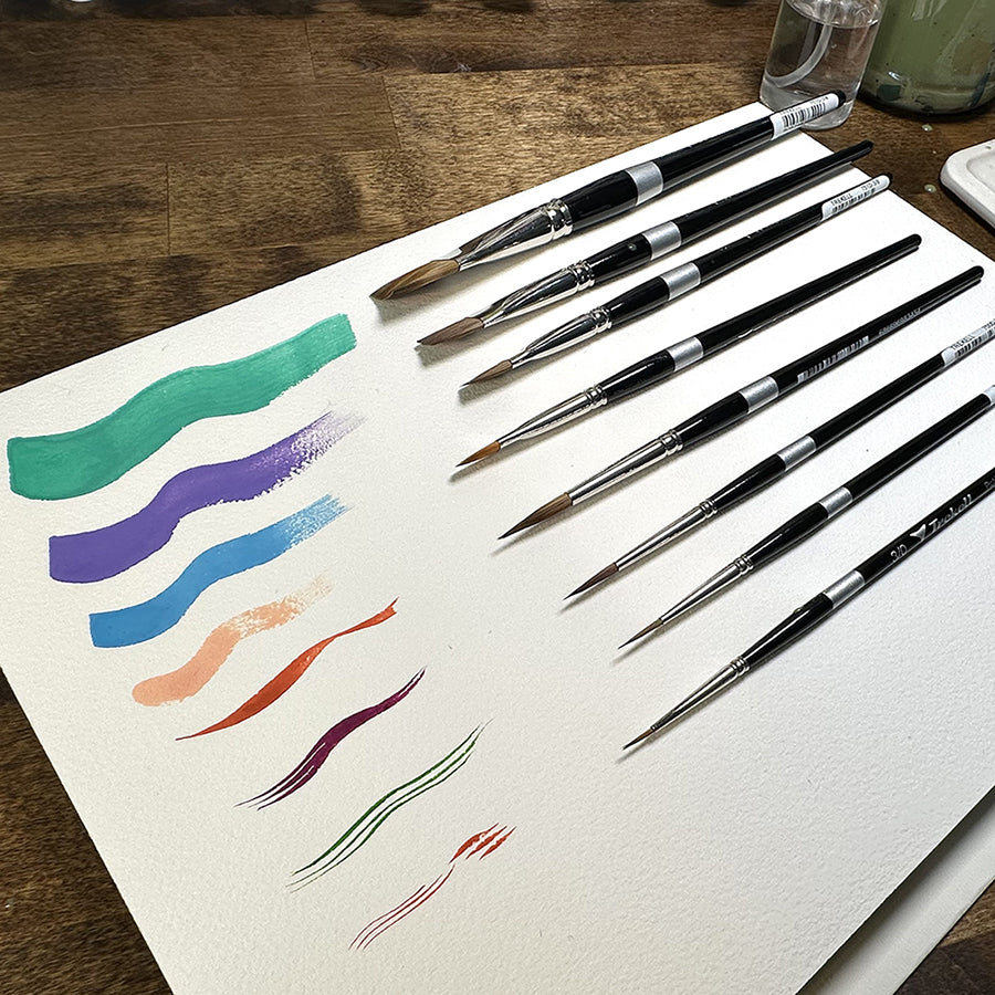 Stephanie Buscema brushes beside green, purple, blue, red and black painted strokes on white paper.