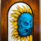 Blue skull surrounded by yellow sunflower petals inside an arched frame.