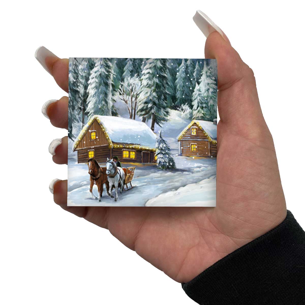 Hand holds a miniature snowy woodland painting with two yellow wooden cabins.
