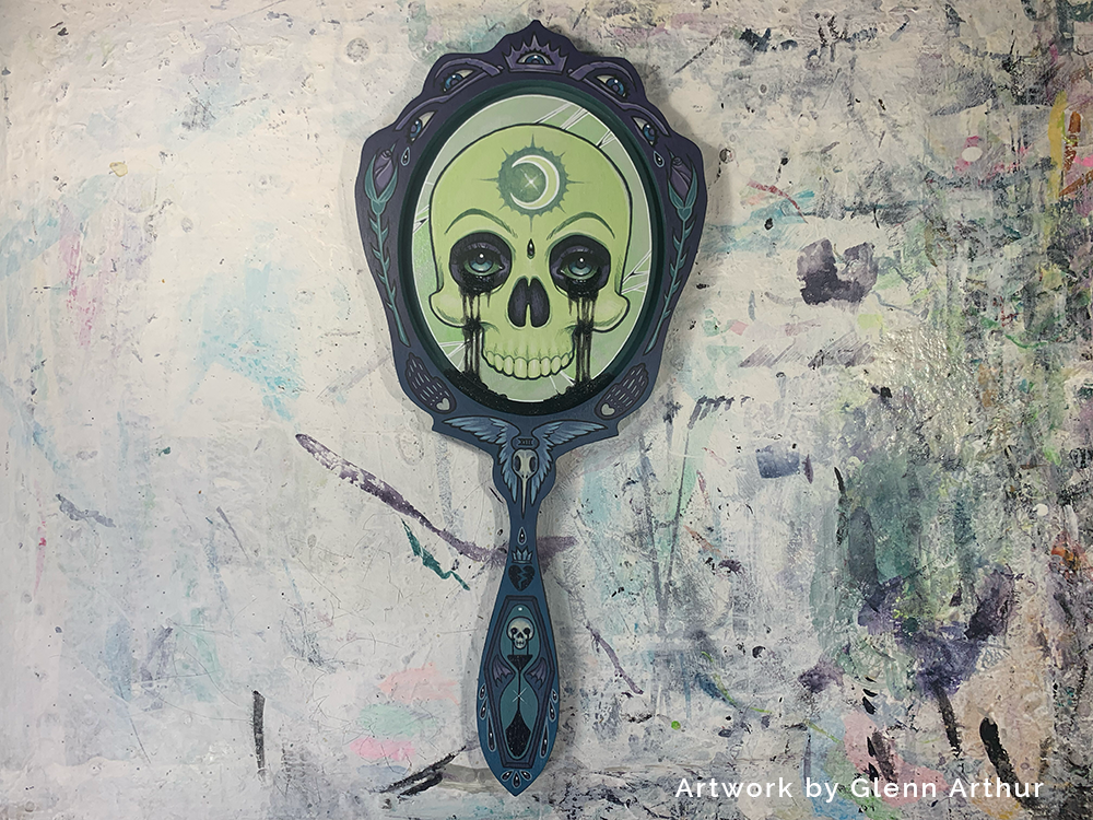 Green skull inside a dark ornate hand-mirror panel, shown upright on a paint-marked surface.