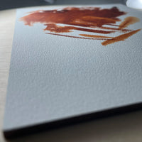 Close-up of a reddish-brown brushstroke on the textured white surface of a gesso panel.