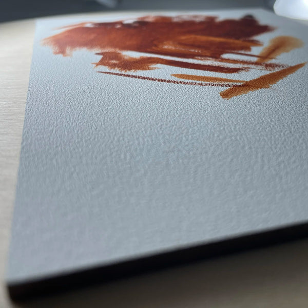 Close-up of a reddish-brown brushstroke on the textured white surface of a gesso panel.