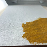 Close-up of an ochre brushstroke on textured white linen.