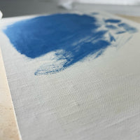 Close-up of a blue brushstroke on pale woven linen.